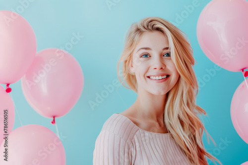 Happy blonde woman with pink balloons against a blue background. Space for text on the right side. A happy birthday concept. © Jane_S