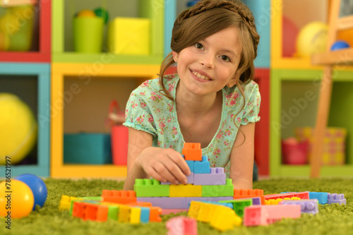 Portrait of cute girl playing with colorful plastic blocks in room