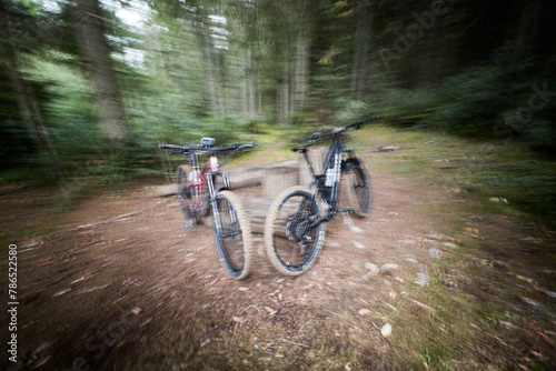 Two modern electric mountain bikes leaning on the fence (no people). Motion blur