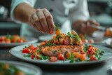 Close-up of a chef's hands adding garnish to a plate of salmon. The chef perfects the dish with herbal garnish and vegetable saute
