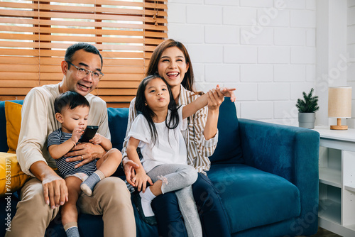 Amidst a modern setting a young family finds happiness and togetherness watching TV at home. The father mother brother and sister enjoy quality family time on the sofa.