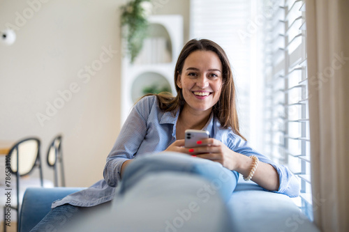 Smiling woman using mobile phone on sofa in living room at home
