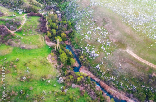 View from the top of a turquoise spring river that flows among green hills and a blooming orchard near Lake Balykty in the Shymkent region of Kazakhstan © Lana Kray