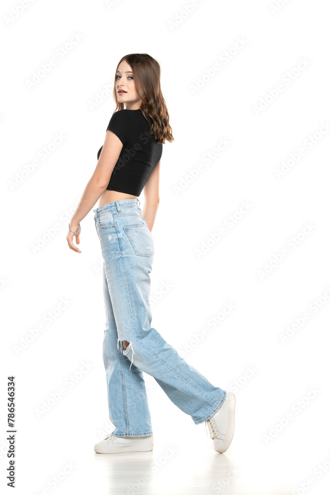 Young female model wearing ripped jeans and black shirt walking on a white background. Side, profilet view Young female model wearing ripped jeans and black shirt walking on a white background. Side, profilet view