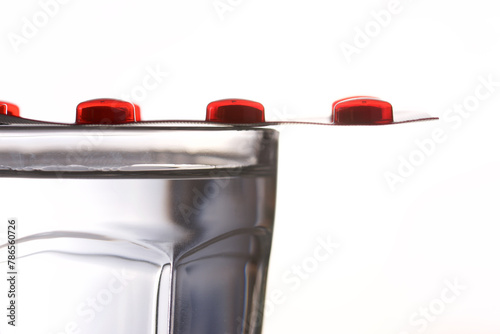 Close-up of a blister pack of red pills on a glass of water