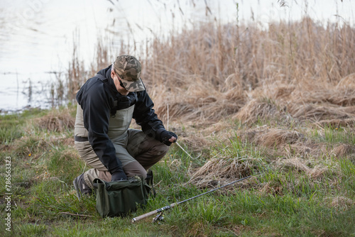 Fisherman in waders and wading boots prepares bait for catching pike in the river photo