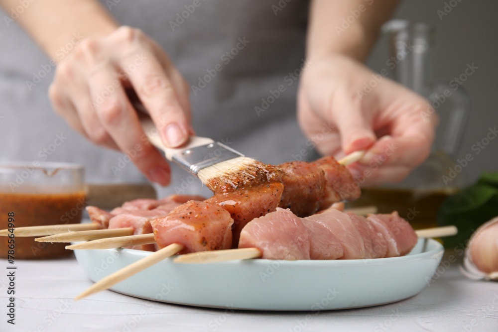Woman spreading marinade onto raw meat with basting brush at table, closeup
