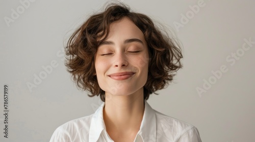 Portrait of a shy female corporate intern smiling with eyes shut against grey background photo