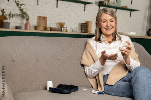 Фотография Good-looking mid aged woman sitting on the sofa and making blood sugar test