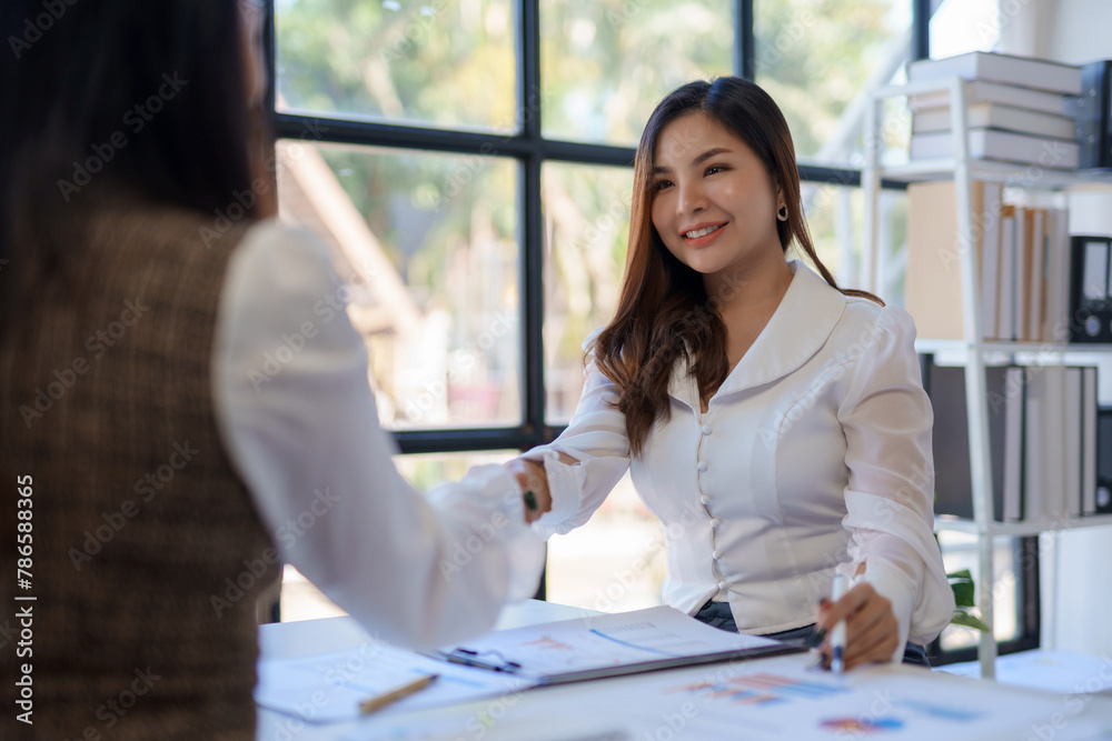 Obraz premium Confident businesswomen shaking hands over a desk in the office.