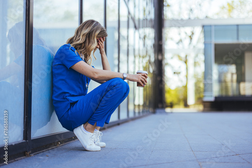 Tired nurse sits on floor outdoors of the medicine clinic after a hard dutty. Exhausted tired doctor or nurse. Clinic and hospital medical stuff working over hours. Overworked professional.  photo