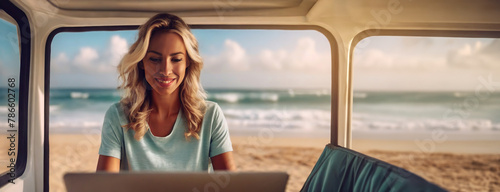 A woman works on her laptop in a van at the beach. Her focused demeanor contrasts the leisurely beach waves and sunny ambiance outside her mobile office.