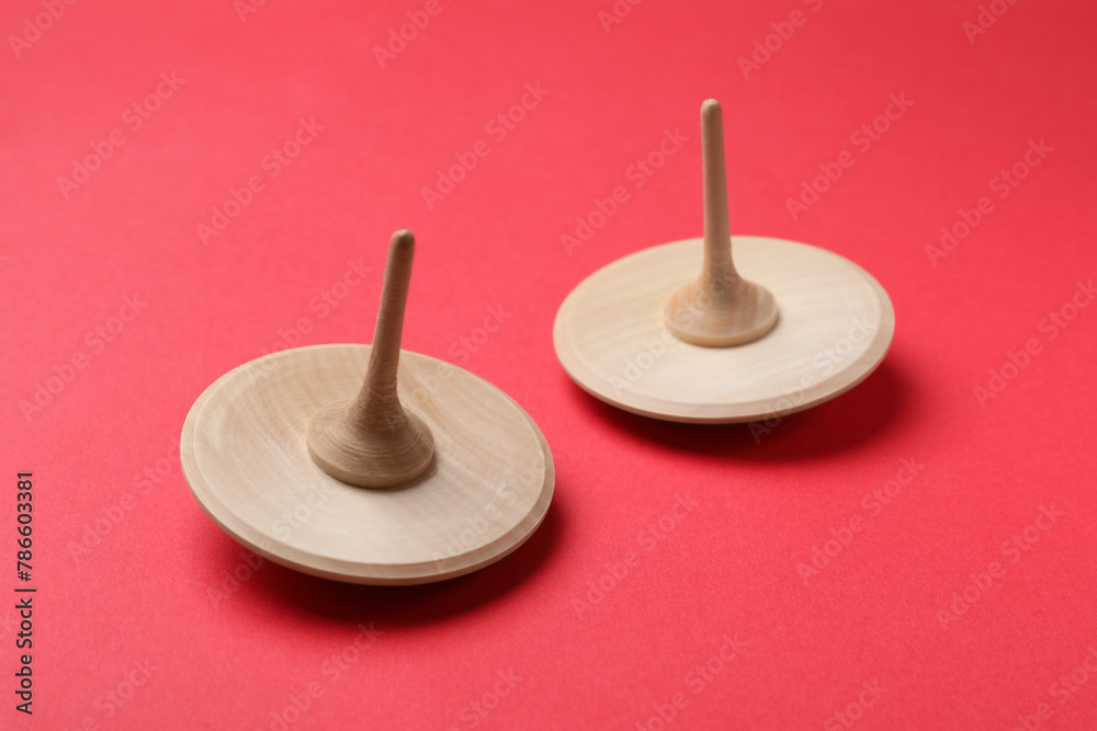 Two wooden spinning tops on red background, closeup
