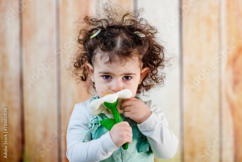 Adorable girl with curly hair .smelling artificial chamomile in front of wooden background