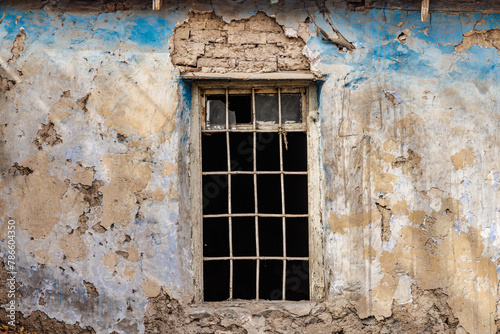 Weathered blue wall with barred window. Vintage window on peeling blue.