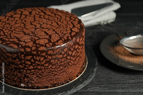 Delicious chocolate truffle cake and cocoa powder on black wooden table, closeup