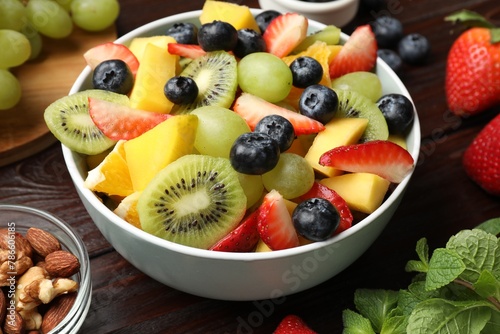 Tasty fruit salad in bowl and ingredients on wooden table  closeup