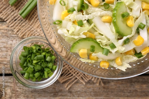 Tasty salad with Chinese cabbage, corn and cucumber in bowl on wooden table, flat lay