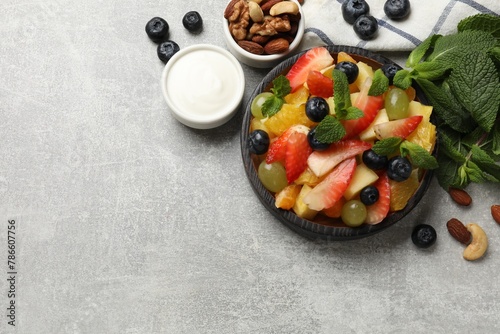 Delicious fruit salad in bowl, berries, nuts and fresh mint on grey table, flat lay. Space for text