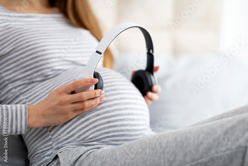 Expecting mother holding headphones over belly, cropped photo