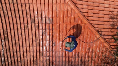 A person outdoors cleaning the red clay roof using a high pressure washer. Professional washing house tiles with water hose.