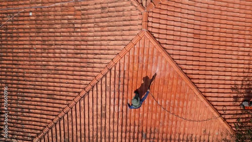 A person outdoors cleaning the red clay roof using a high pressure washer. Professional washing house tiles with water hose.