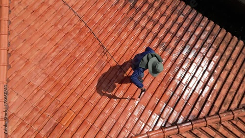 A person outdoors cleaning the red clay roof using a high pressure washer. Professional washing house tiles with water hose.