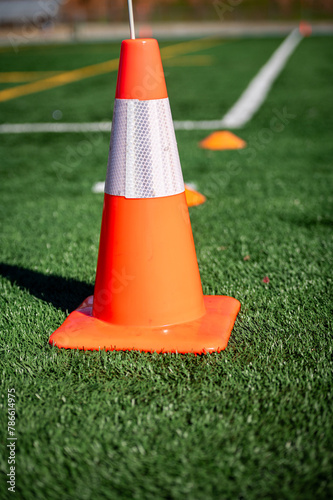 Photo of an orange pylon with white reflector tape on an artificial turf playing field