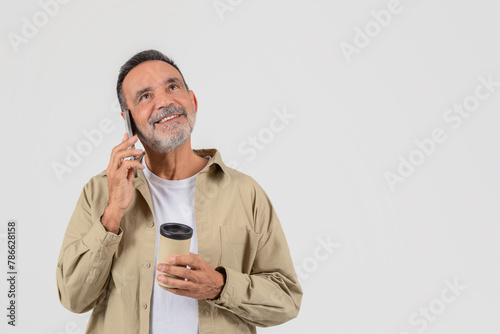 Senior man talking on phone holding coffee cup © Prostock-studio