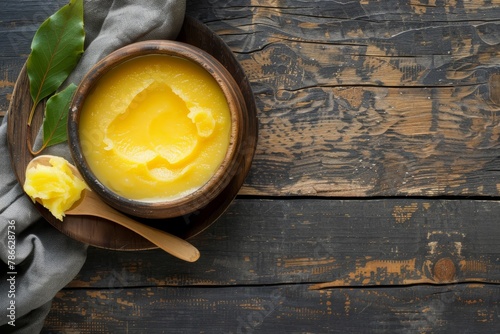 Ghee in wooden bowl with spoon and bay leaves on rustic table. Culinary photography with natural ingredients concept. Close-up shot of clarified butter with copy space.