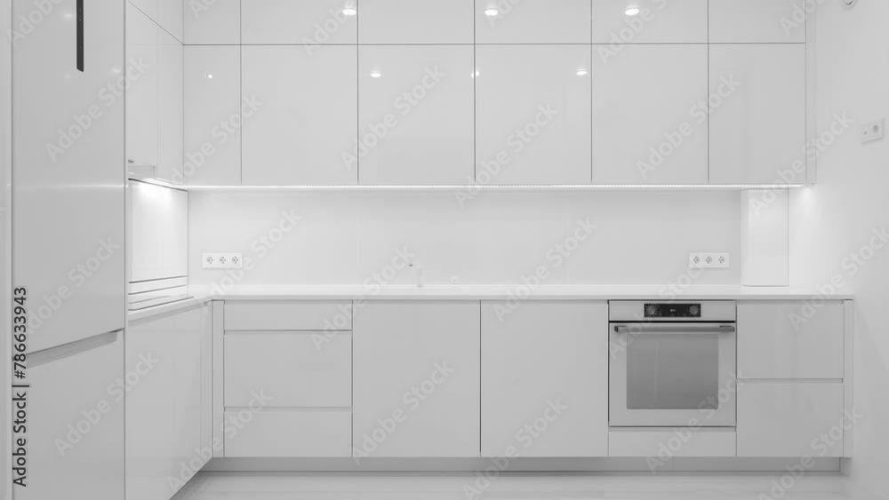 Front view of a modern luxury trendy snow white kitchen with many cabinets, glossy lacquered facades and integrated handle. Nobody Front view of a modern luxury trendy snow white kitchen with many cabinets, glossy lacquered facades and integrated handle. Nobody