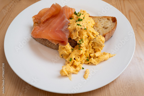 Scrambled eggs sprinkled with chives on sourdough toast with smoked salmon on a white plate.