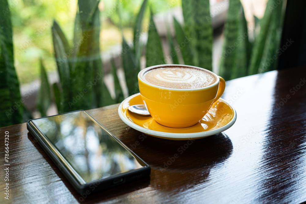 Hot coffee latte with latte art milk foam in cup mug,smartphone on wood desk on top view. As breakfast In a coffee shop at the cafe,during business work concept,vintage style
