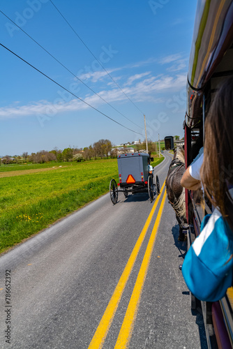 A view from a tour wagon captures an Amish buggy traveling down a rural road in Lancaster, PA, showcasing Amish transportation and the picturesque countryside. High quality photo. US