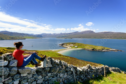 Jeune homme assis sur un muret de pierres  admirant la vue sur la presqu'île Ard Neakie Lime Kilns au bord du Loch Eriboll en Ecosse au printemps photo