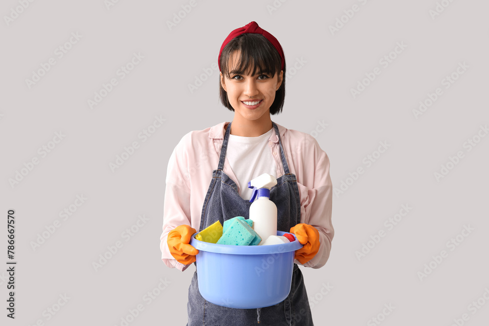Young woman with cleaning supplies on light background Young woman with cleaning supplies on light background