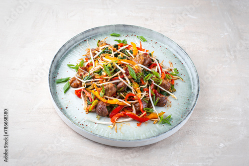 Traditional Asian wok spinach with chestnuts, pepper strips and soy sprouts served as close-up in a Nordic design plate with copy space