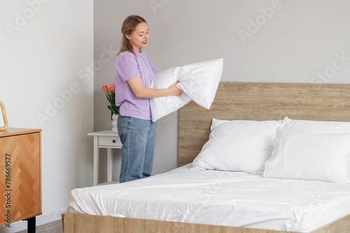 Pretty young woman putting pillow on bed in bedroom