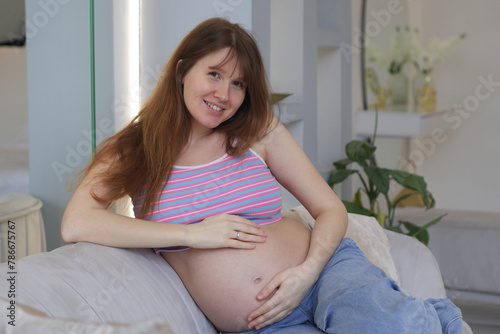 Happy smiling pregnant woman looking camera by touching or feeling tummy - concept of Expecting mother Expecting Baby, Prenatal connection and motherhood. Pregnant Woman Belly. Pregnancy. Baby Shower 