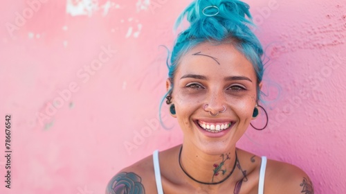 Joyful woman with blue hair and colorful tattoos against pink wall. Cheerful urban portrait.