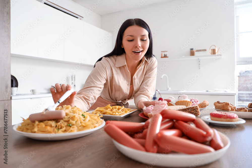 Young woman at table with unhealthy food in kitchen. Overeating concept