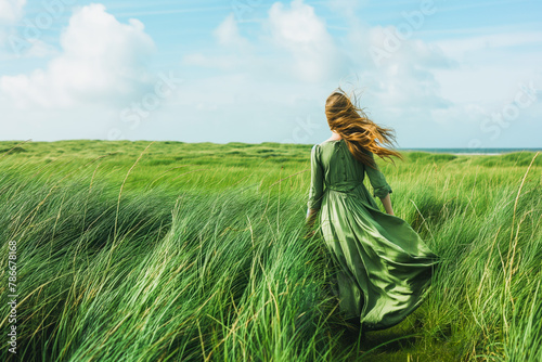 Woman walking in green windy field with tall grass wearing long dress