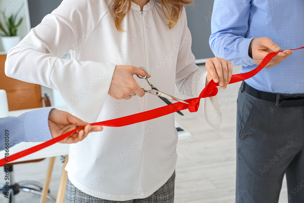 Business people cutting red ribbon in office, closeup