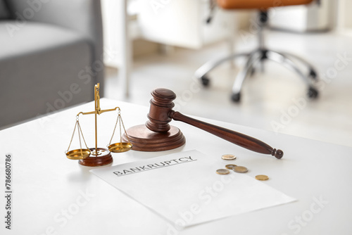 Paper with word BANKRUPTCY, justice scales, judge's gavel and coins on table in office, closeup
