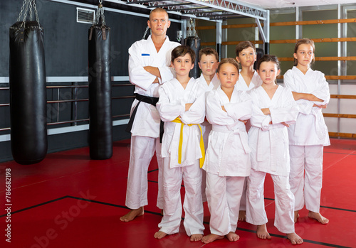 Young sportive children with their male instructor posing in karate class before training