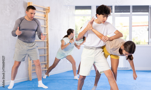 Girls and boys learns to do power grip with trainer during a self-defense lesson in the gym