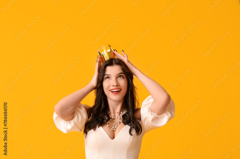 Beautiful young woman in stylish prom dress and paper crown on yellow background Beautiful young woman in stylish prom dress and paper crown on yellow background
