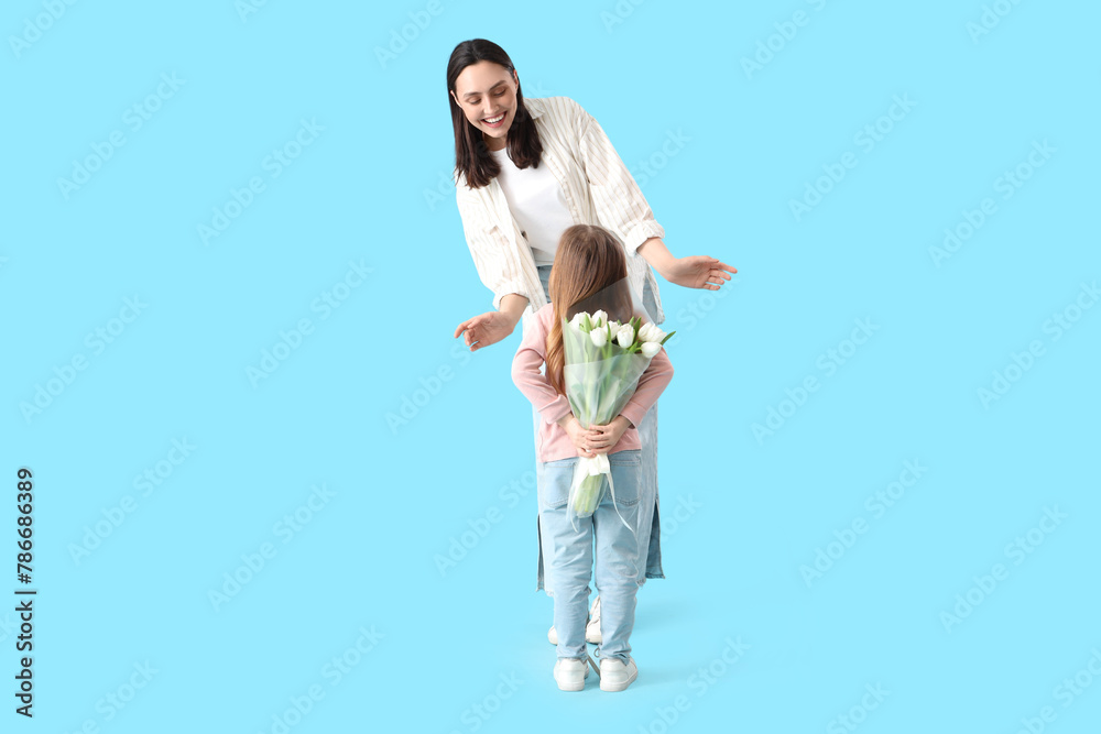 Young woman receiving tulips from her little daughter on blue background. Mother's Day celebration Young woman receiving tulips from her little daughter on blue background. Mother's Day celebration