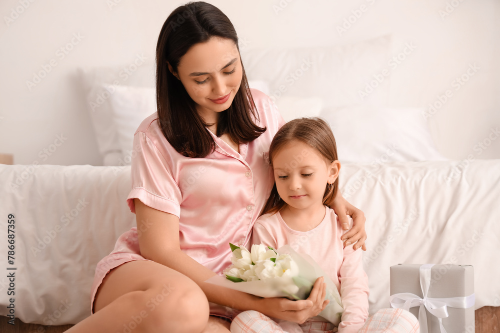 Happy mother with tulips hugging her cute little daughter in bedroom on holiday Happy mother with tulips hugging her cute little daughter in bedroom on holiday
