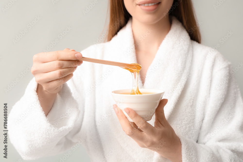 Beautiful young happy woman holding bowl and spatula with sugaring paste on grey background, closeup Beautiful young happy woman holding bowl and spatula with sugaring paste on grey background, closeup